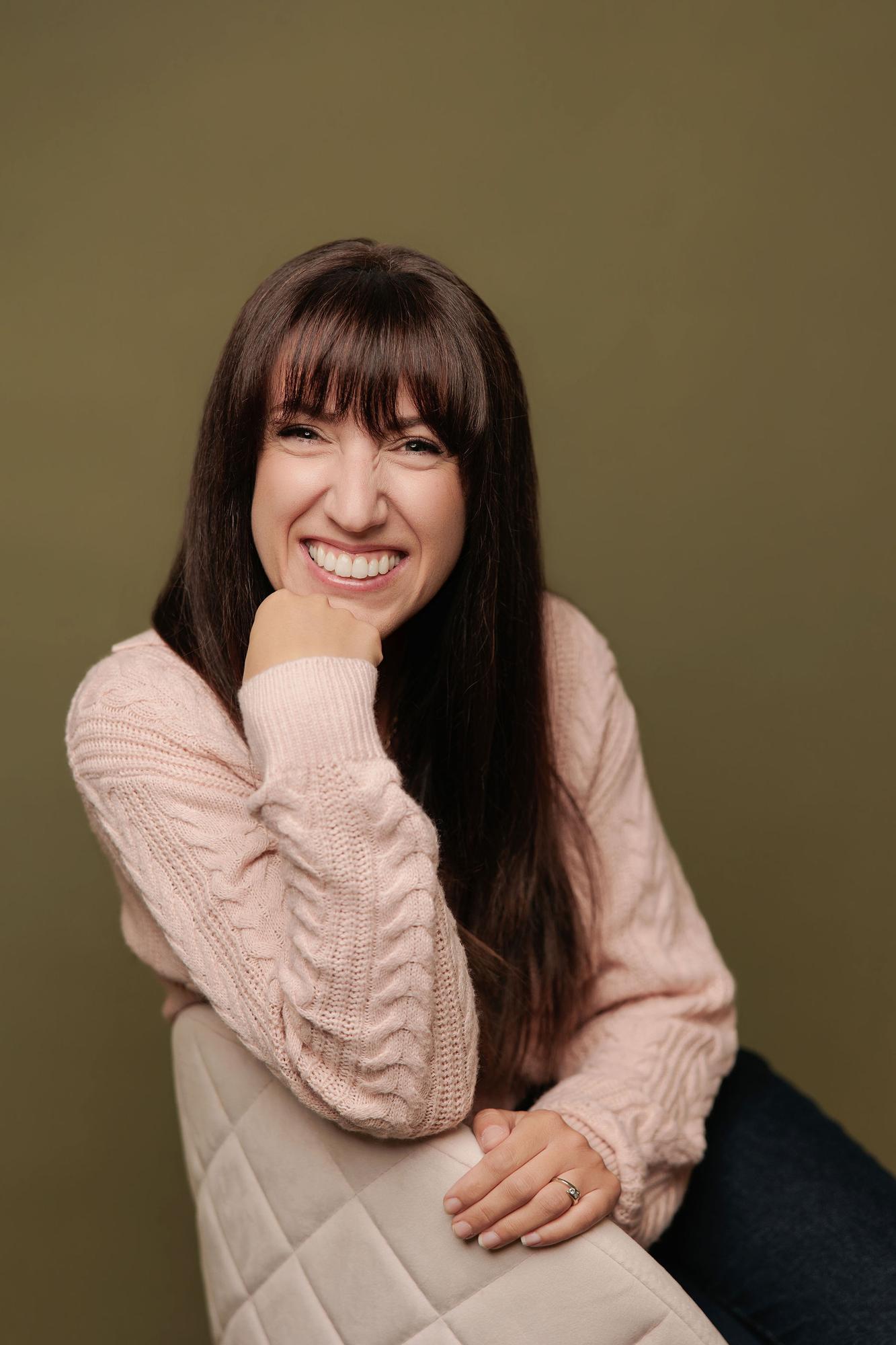 A woman with long dark hair and a pink sweater laughs in our Calgary photography studio, showcasing the warm, authentic style of our headshots.