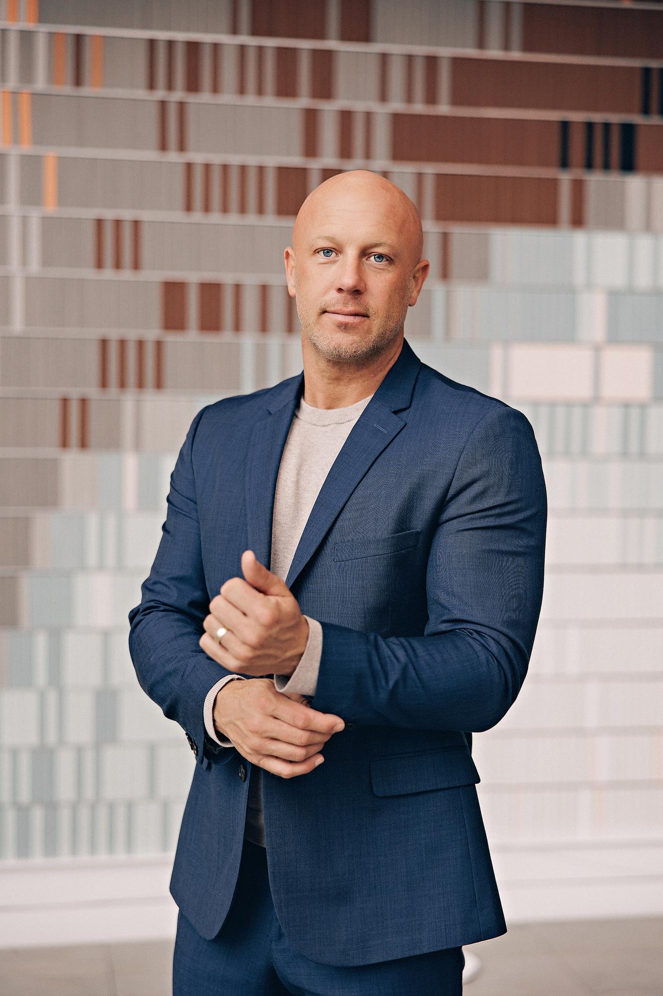 Executive personal branding headshot Calgary: Focused male professional in a navy blue blazer and grey t-shirt adjusting his sleeve in front of a vibrant multicolour striped art installation