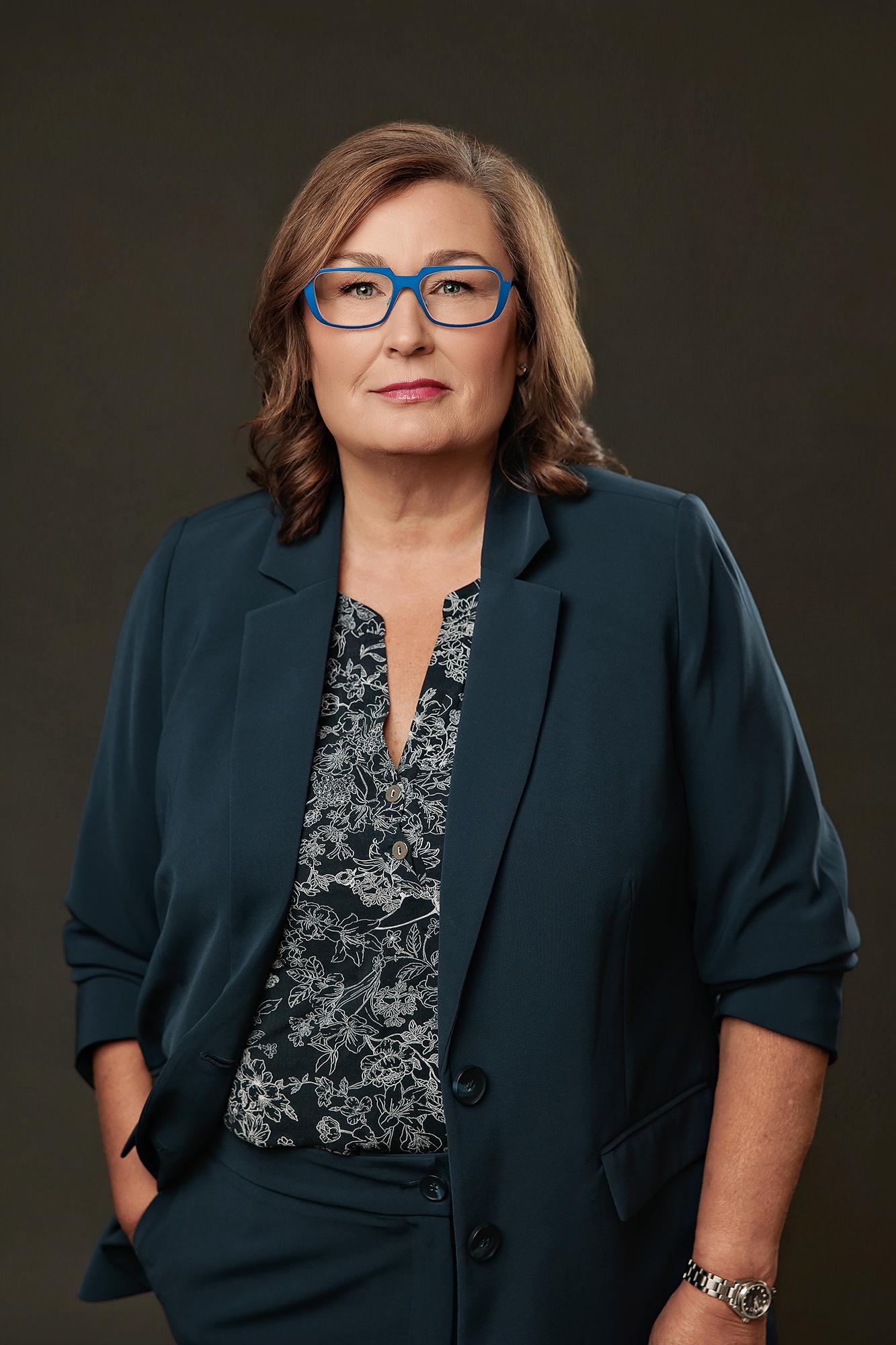 A professional woman with blue glasses wears a teal blazer in this Calgary headshot photography studio session, featuring soft, flattering studio lighting.