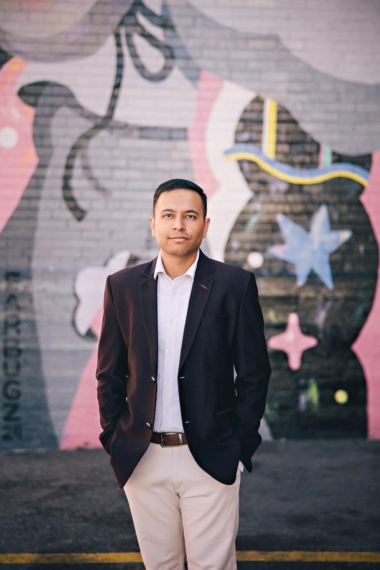 Urban professional headshot Calgary: Confident man in a navy blazer and white shirt with hands in pockets standing in front of a colourful abstract unicorn street mural