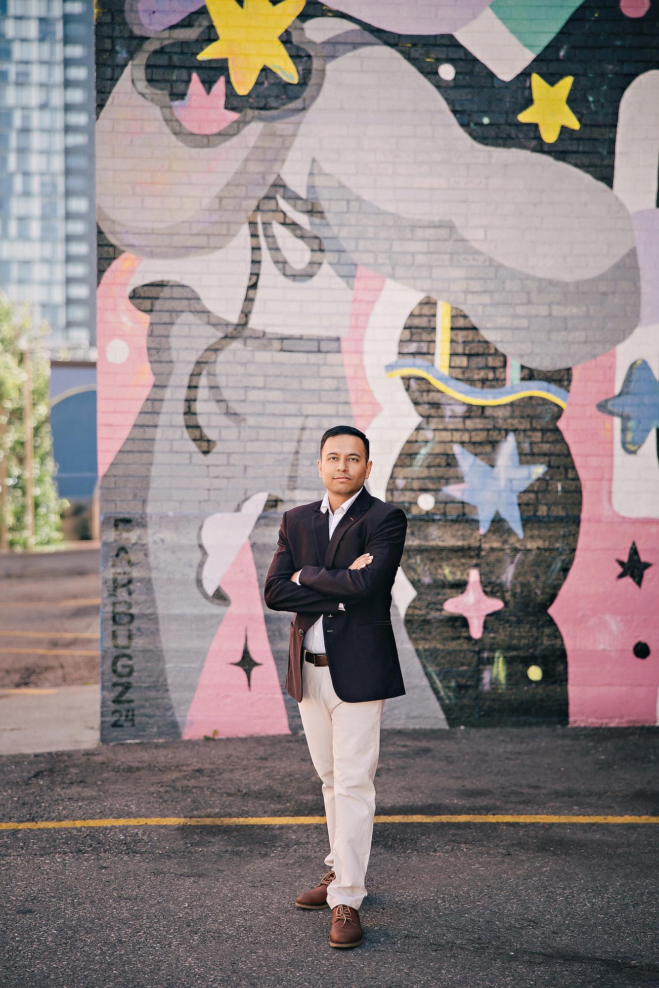 Full-length urban personal branding portrait Calgary: Powerful man in a navy blazer and khaki trousers standing with arms crossed in front of a large colourful unicorn street mural