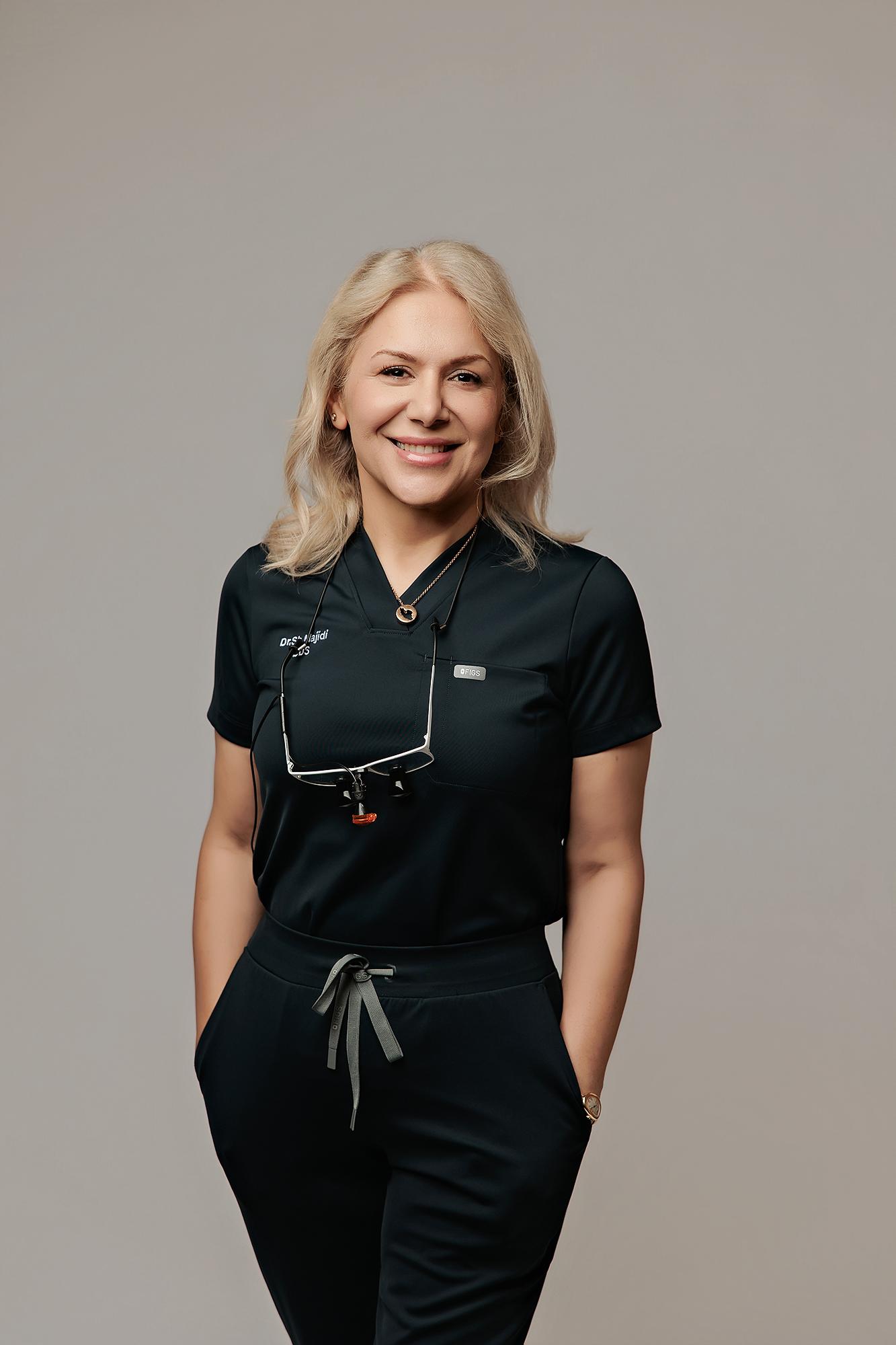 A smiling female dentist in black scrubs poses for a professional headshot at our Calgary photography studio, featuring soft studio lighting on a neutral backdrop.