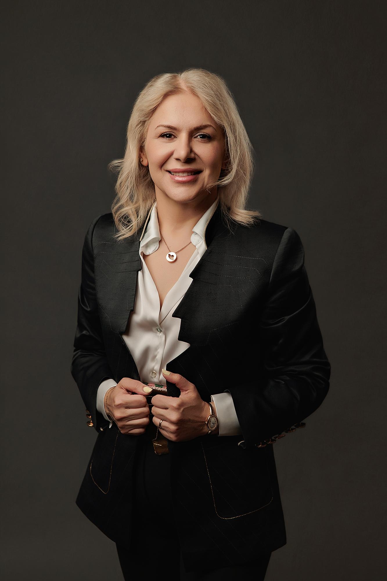 Blonde woman in a black blazer and white shirt smiles confidently for a professional headshot at our Calgary photography studio, featuring soft lighting.