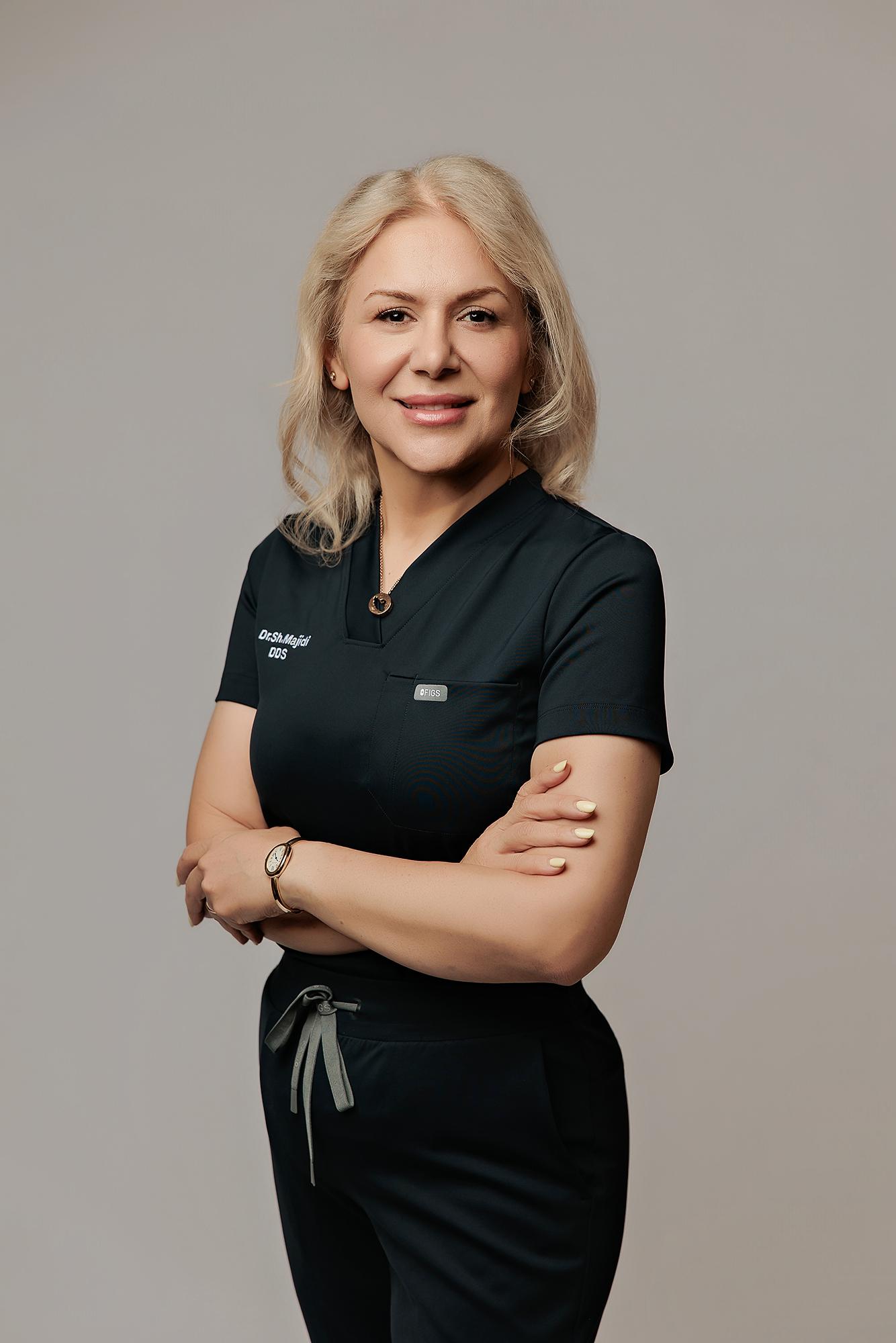 A professional dentist poses with arms crossed in this Calgary studio headshot, featuring soft studio lighting against a neutral grey backdrop.