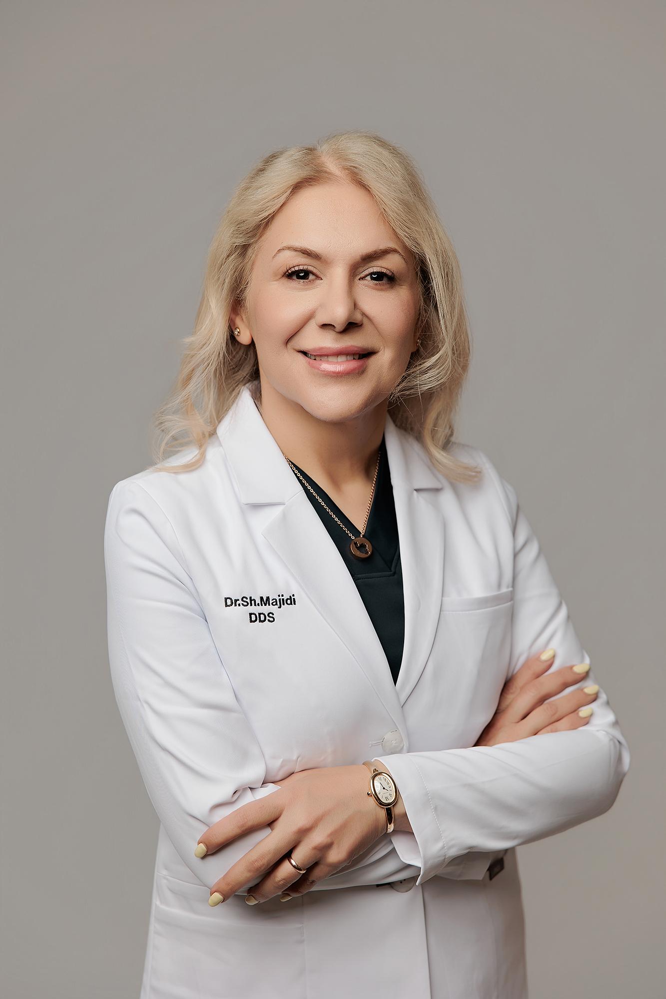 A smiling female dentist in a white lab coat poses with arms crossed for this professional headshot taken at our Calgary photography studio.