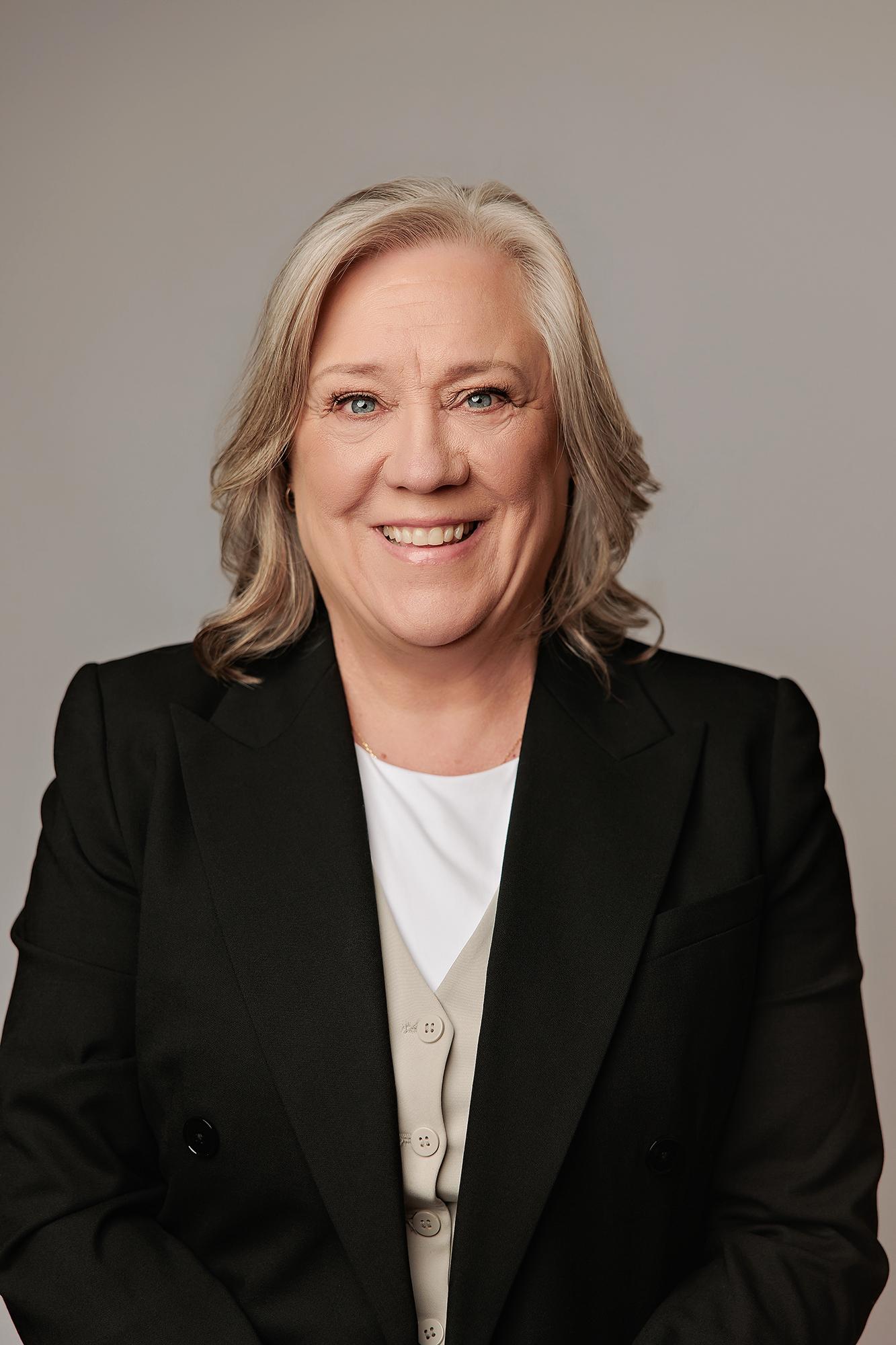 A smiling woman with silver hair wears a professional black blazer in this Calgary headshot photography studio session featuring soft, even lighting.