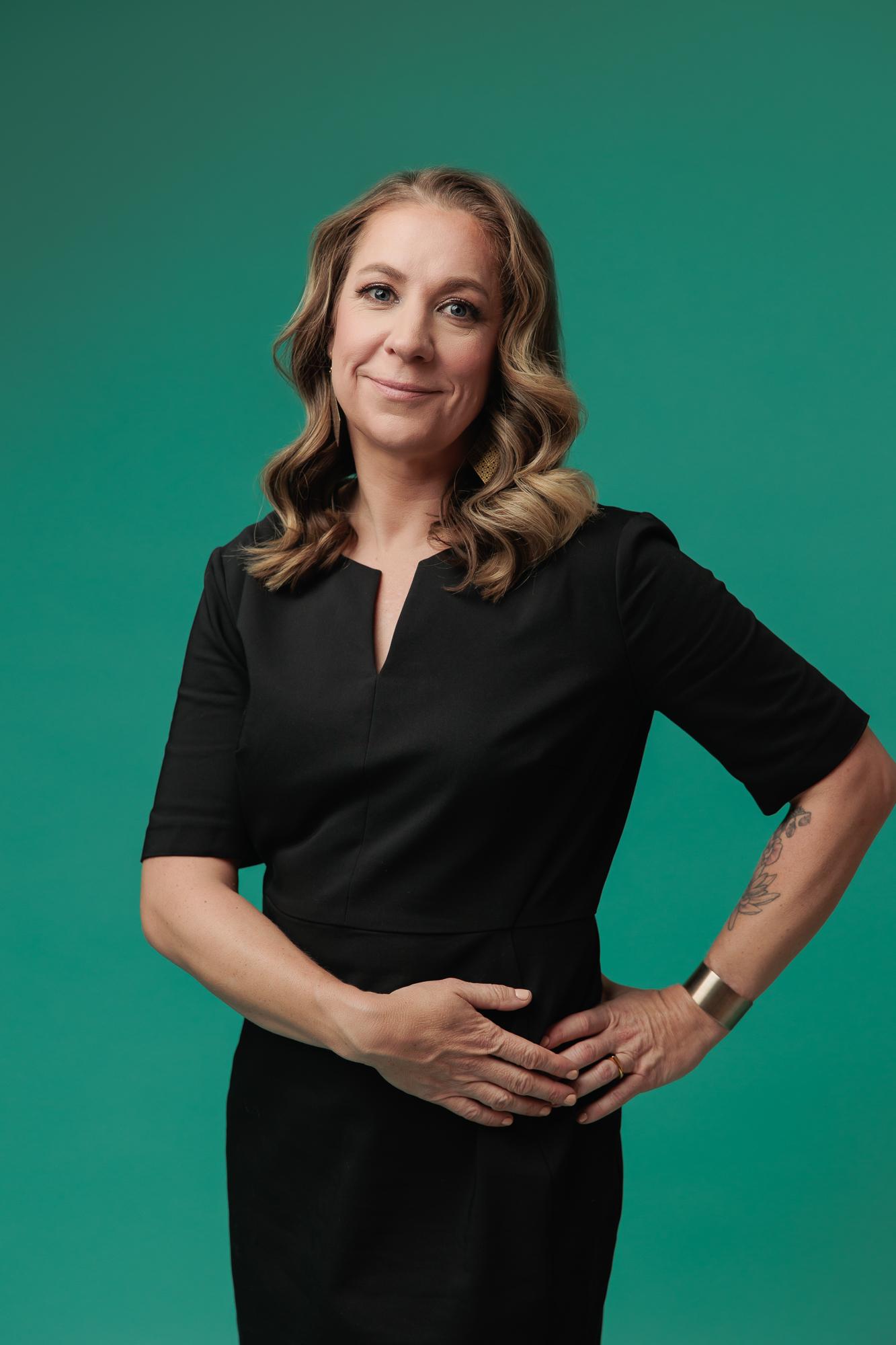 A professional woman with wavy hair wears a black dress in this Calgary headshot session, featuring soft studio lighting against a vibrant green backdrop.