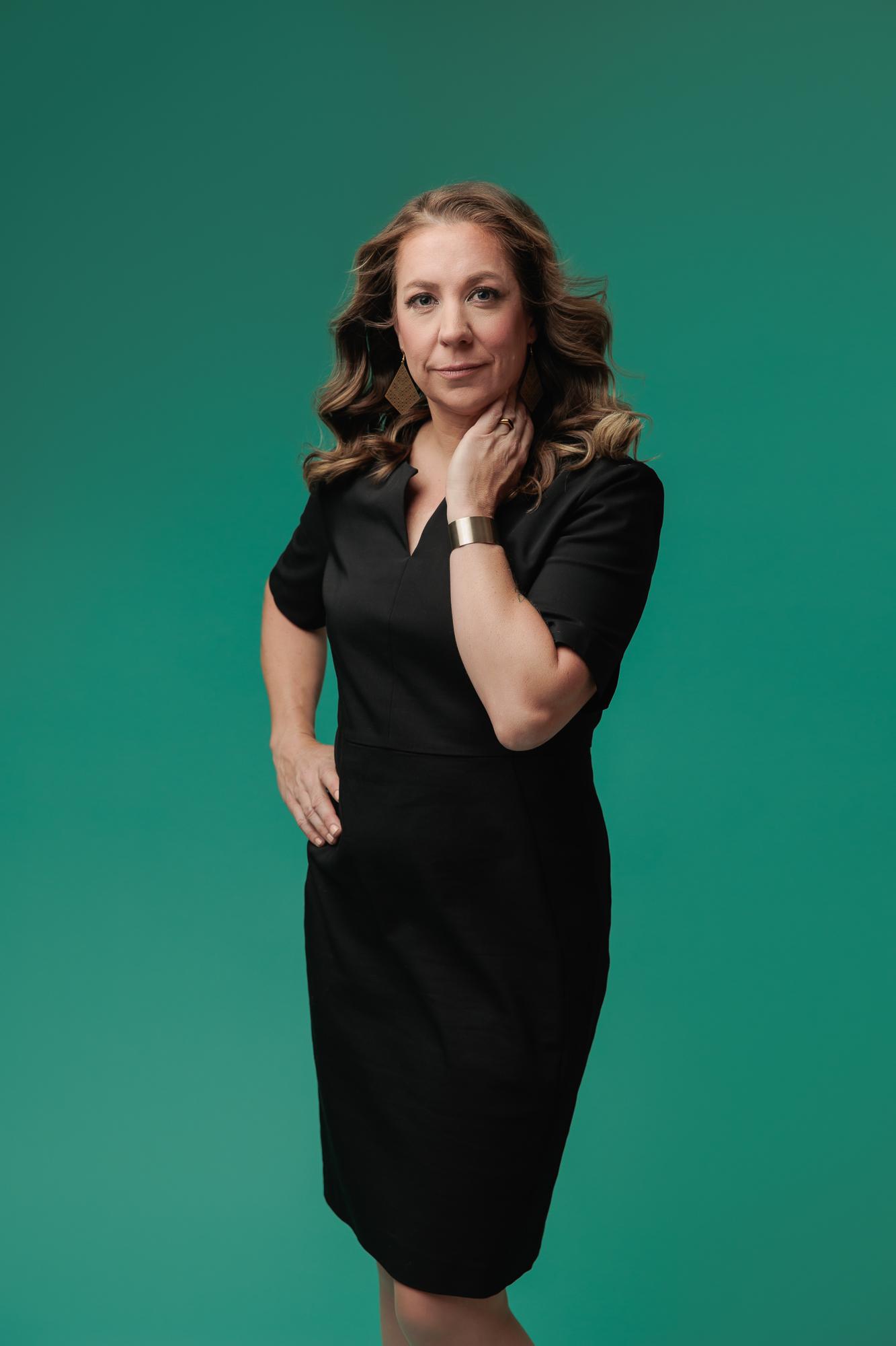 A woman in a black dress poses confidently for a professional headshot at a Calgary studio, featuring soft lighting against a vibrant green backdrop.