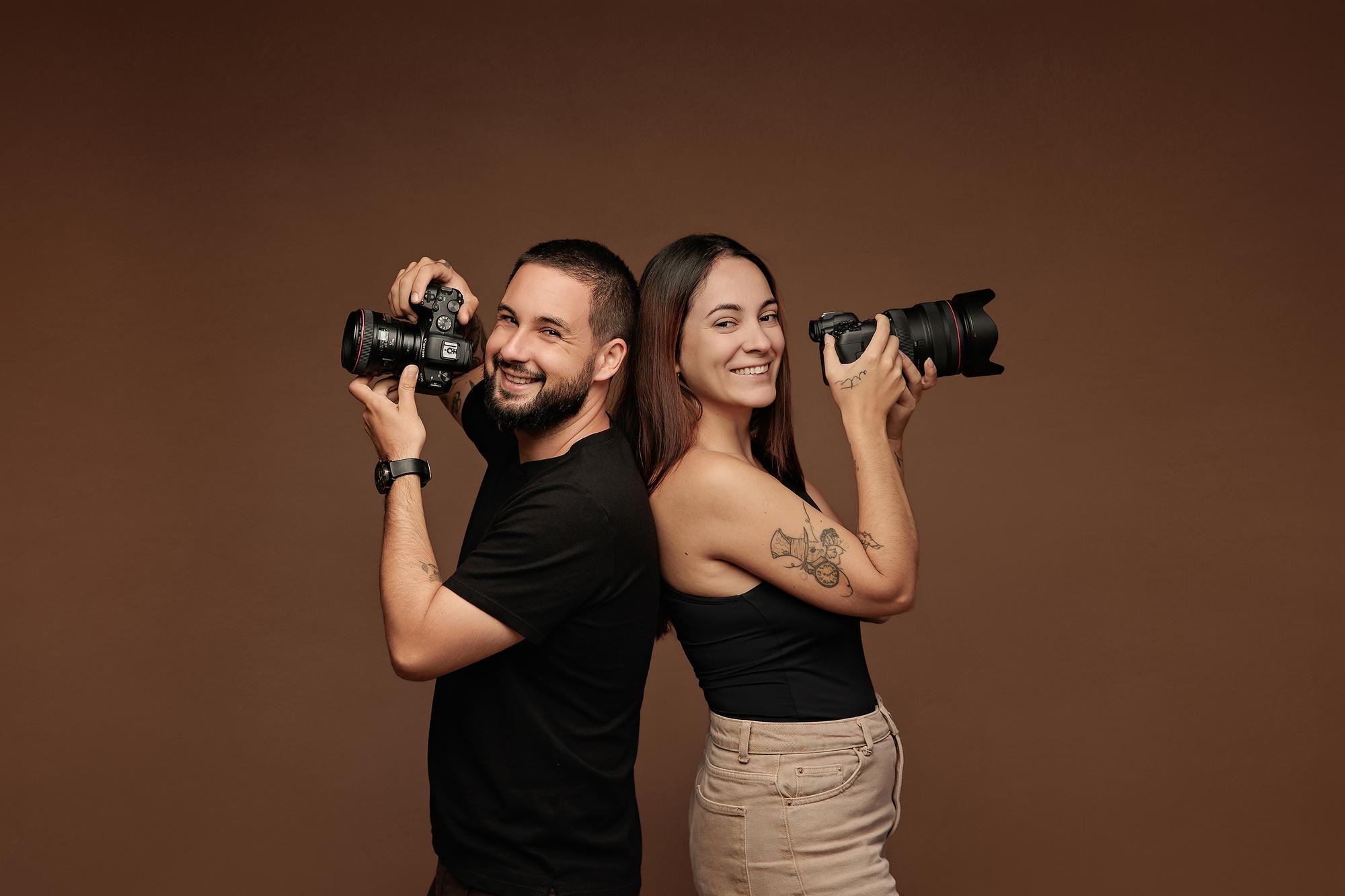 Two smiling photographers stand back-to-back holding cameras in this Calgary studio, showcasing the professional team behind our headshot sessions.