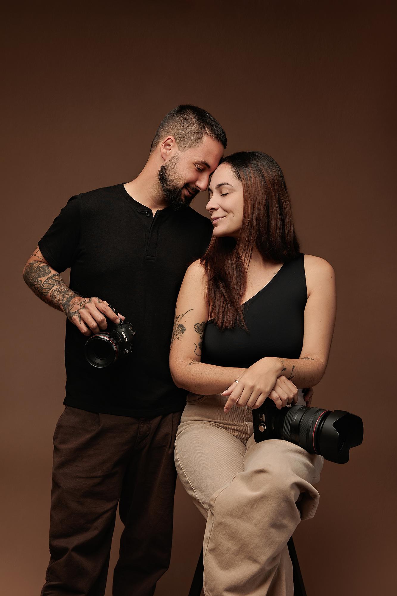 A professional Calgary photography team poses with cameras in a studio setting, featuring soft lighting against a warm brown backdrop for a modern look.