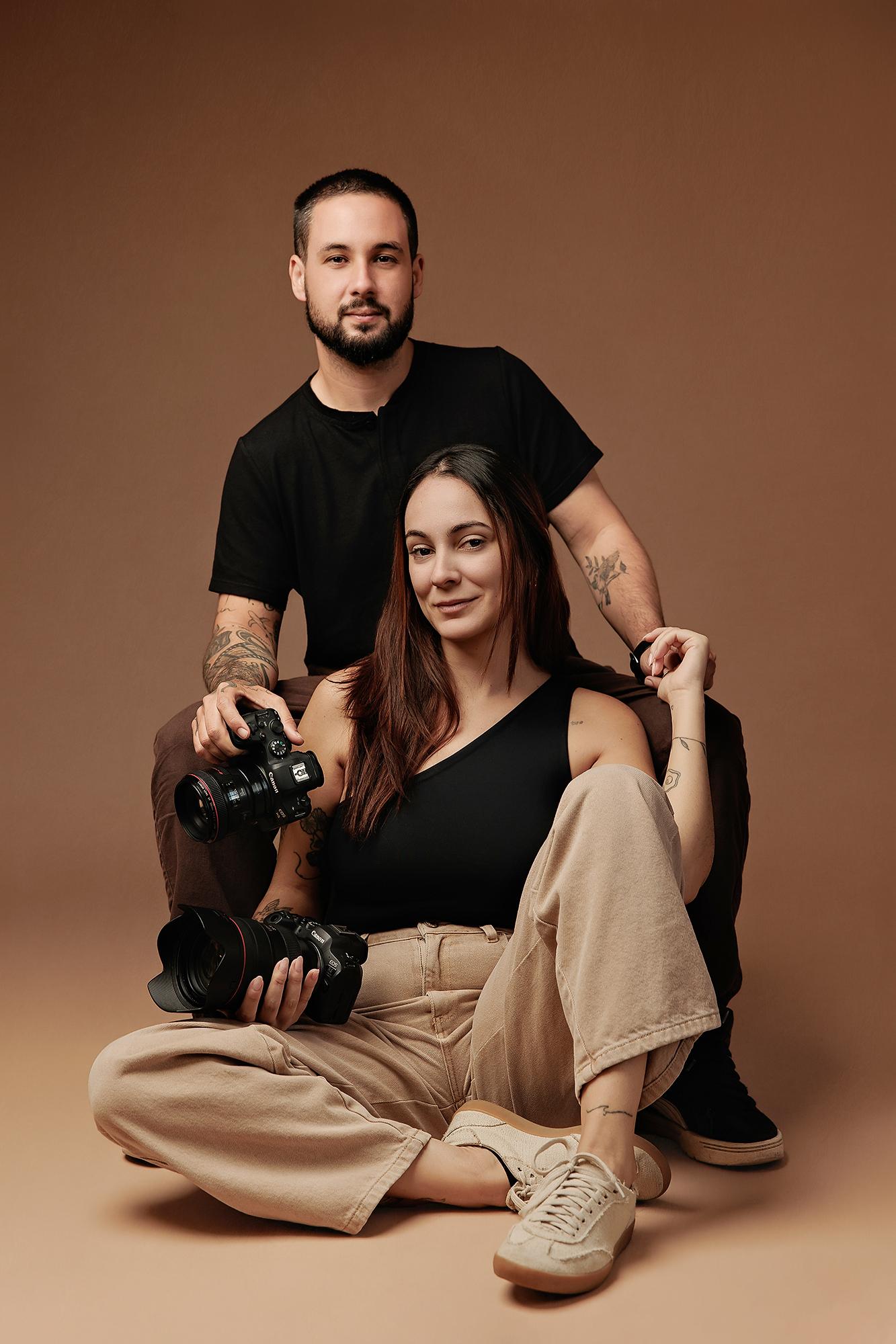 A professional Calgary photography duo poses with cameras in a studio, showcasing the collaborative spirit behind our expert team and branding sessions.