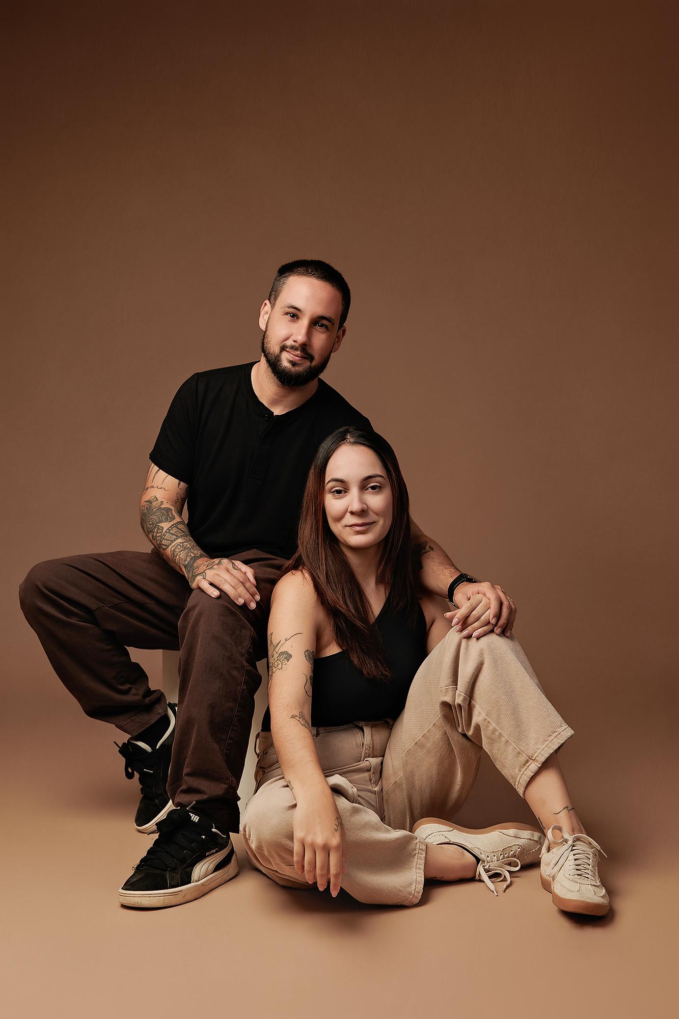 A man and woman pose for a personal branding session at our Calgary photography studio, featuring soft studio lighting against a warm mocha backdrop.
