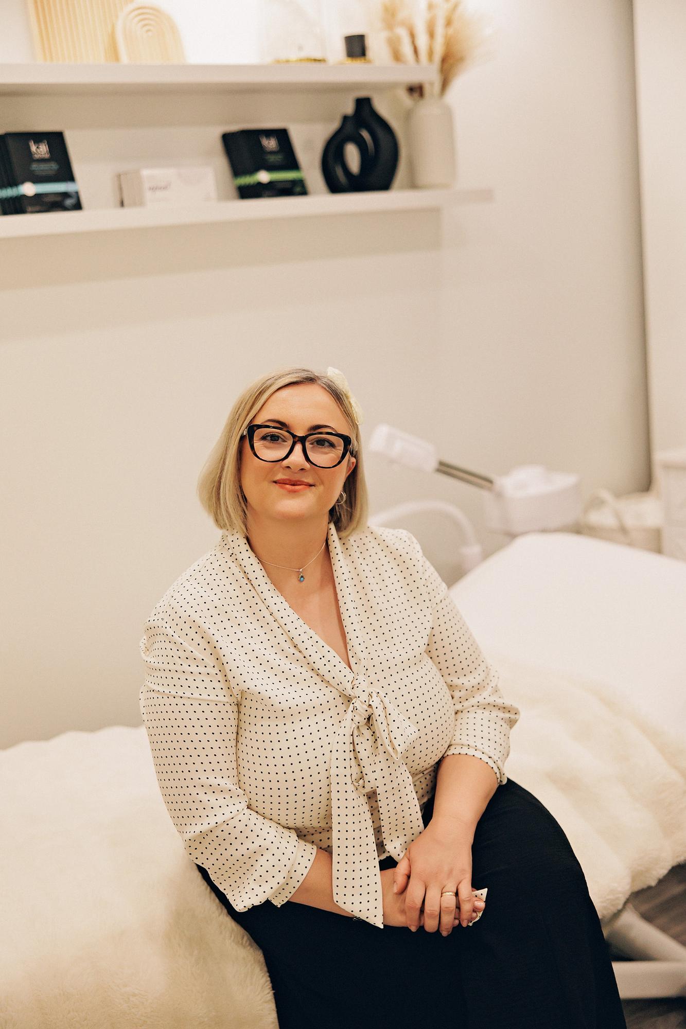 A woman with blonde hair and glasses wears a polka dot blouse in this Calgary personal branding session, captured in a bright, professional studio.