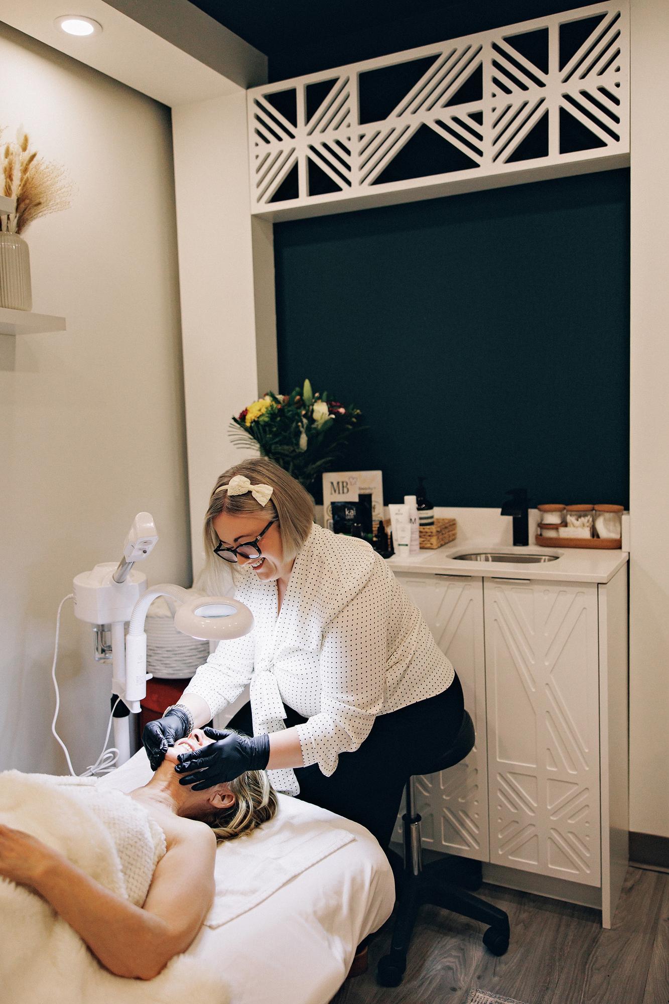 A smiling esthetician in a polka-dot blouse performs a facial in this Calgary personal branding session, captured with soft studio lighting and detail.
