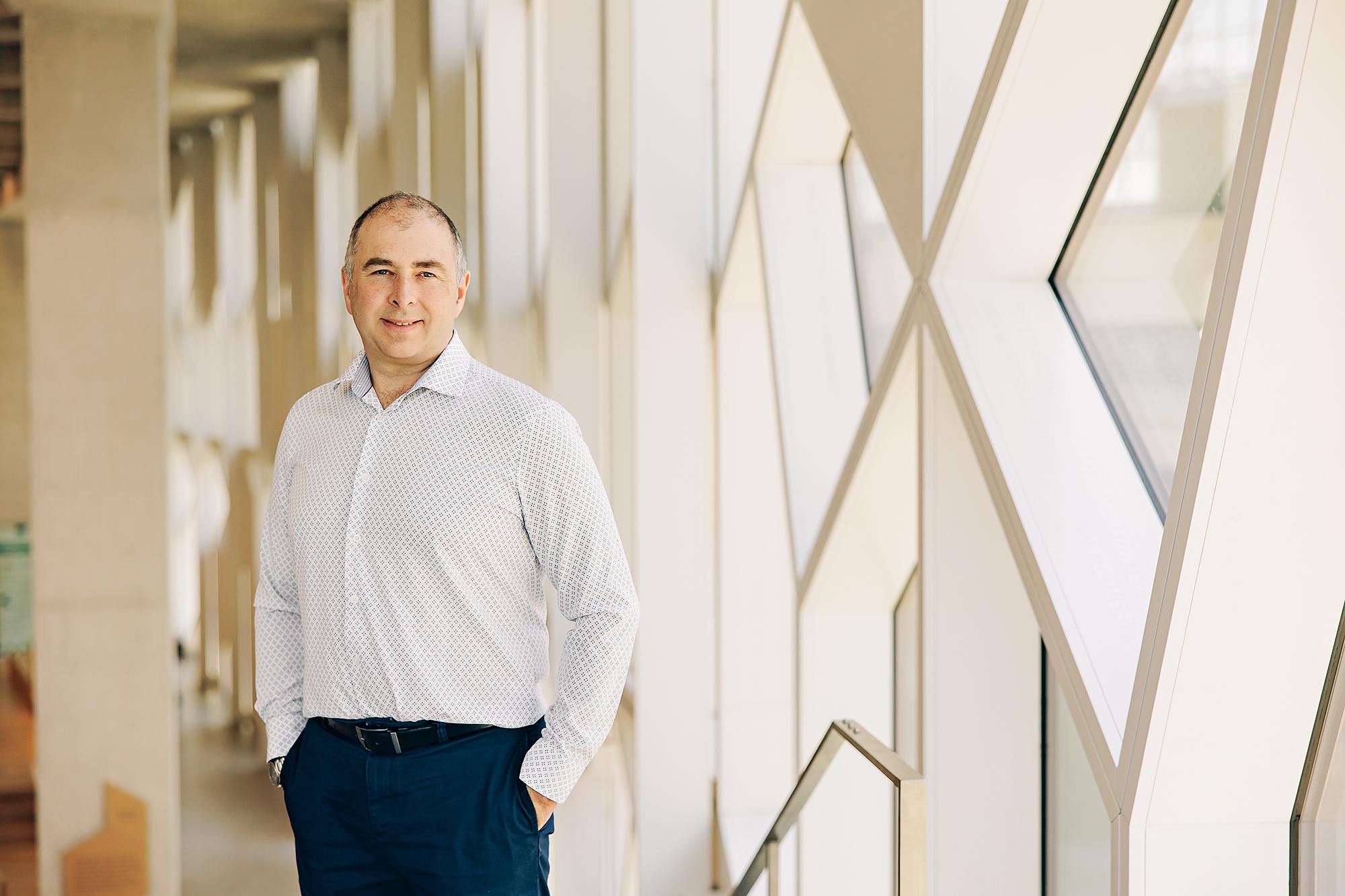 A smiling professional in a patterned shirt stands in a bright Calgary studio, showcasing the clean aesthetic of a modern corporate headshot.