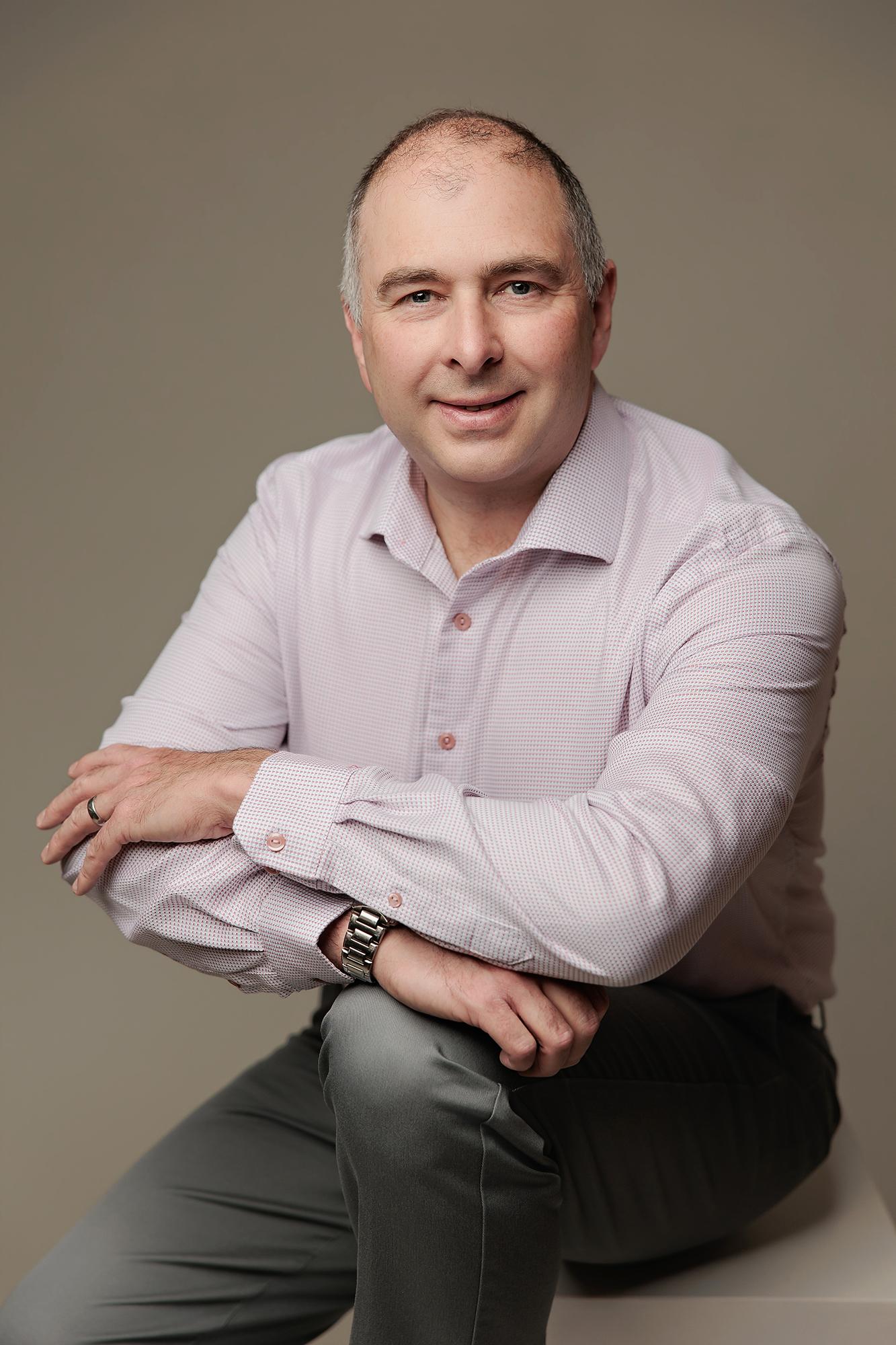 A smiling man in a light pink button-down shirt poses for a professional headshot at our Calgary photography studio with soft, flattering lighting.