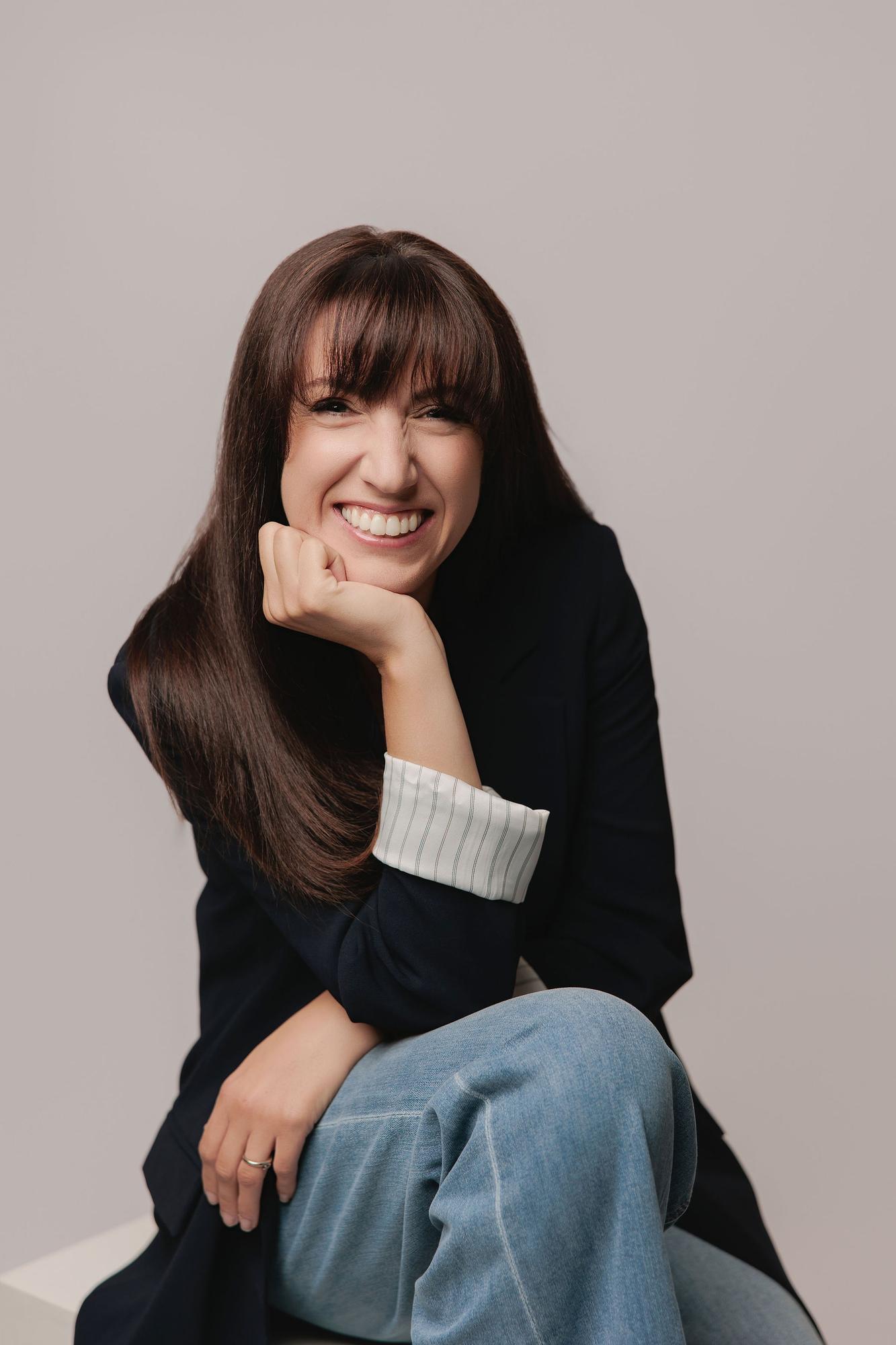 A woman with long brown hair smiles broadly while resting her chin on her hand, showcasing a relaxed personal branding style by a Calgary photographer.
