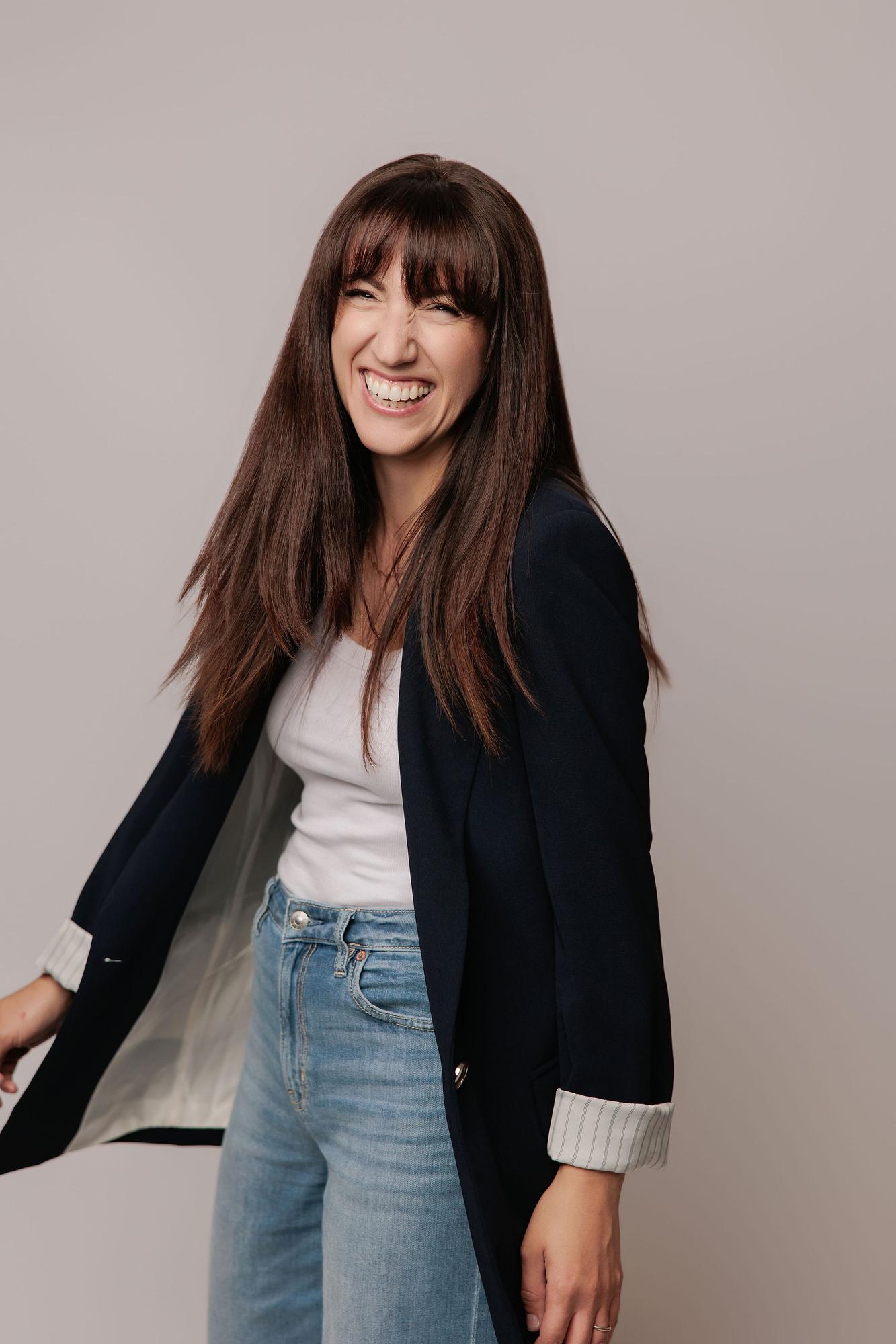 A woman with long brown hair laughs in a navy blazer and jeans, showcasing the authentic personal branding style of our Calgary photography studio.