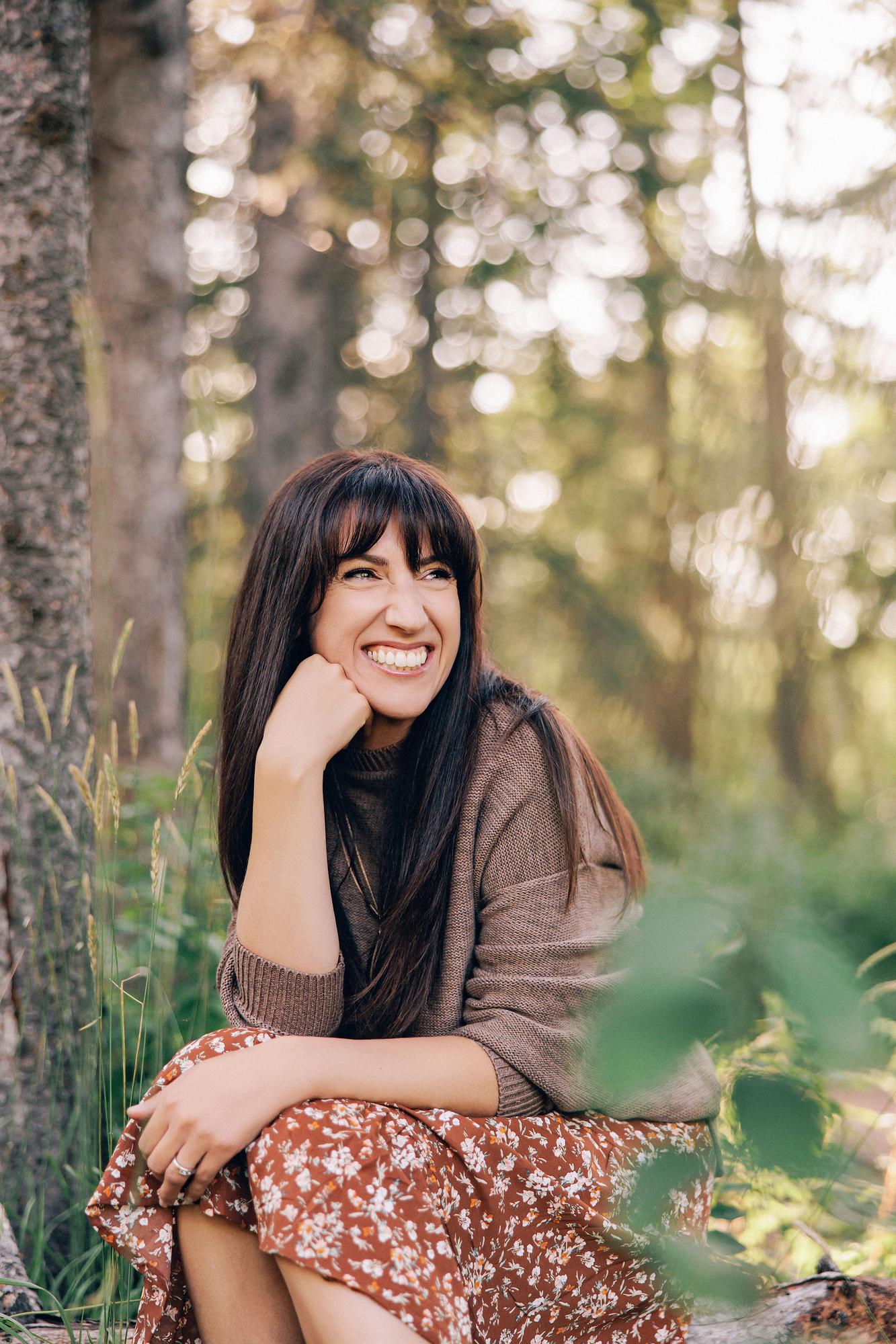 A woman with dark hair laughs in a forest setting, showcasing the natural outdoor style of our Calgary photography studio for personal branding.