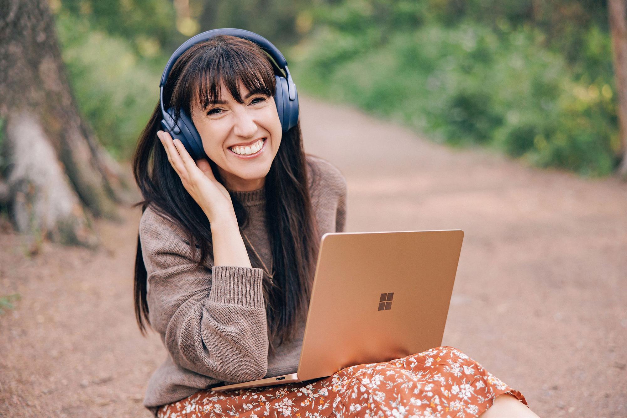 A smiling woman wears headphones and uses a laptop in a park, showcasing the relaxed personal branding style of this Calgary headshot photographer.