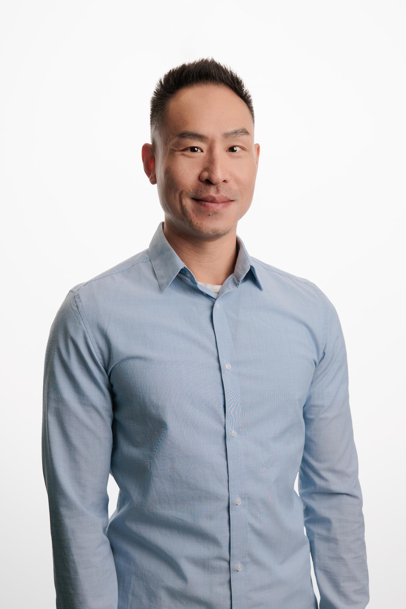 Team headshots Calgary studio: Confident professional man in a light blue shirt in a relaxed three-quarter pose against a white studio background