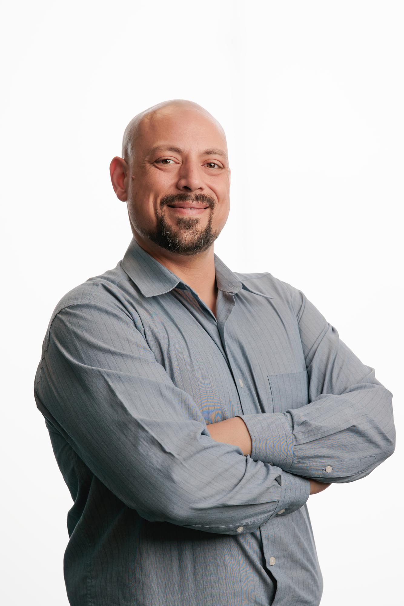 Team headshots Calgary studio: Confident professional man in a grey flannel shirt with arms crossed facing forward against a clean white backdrop